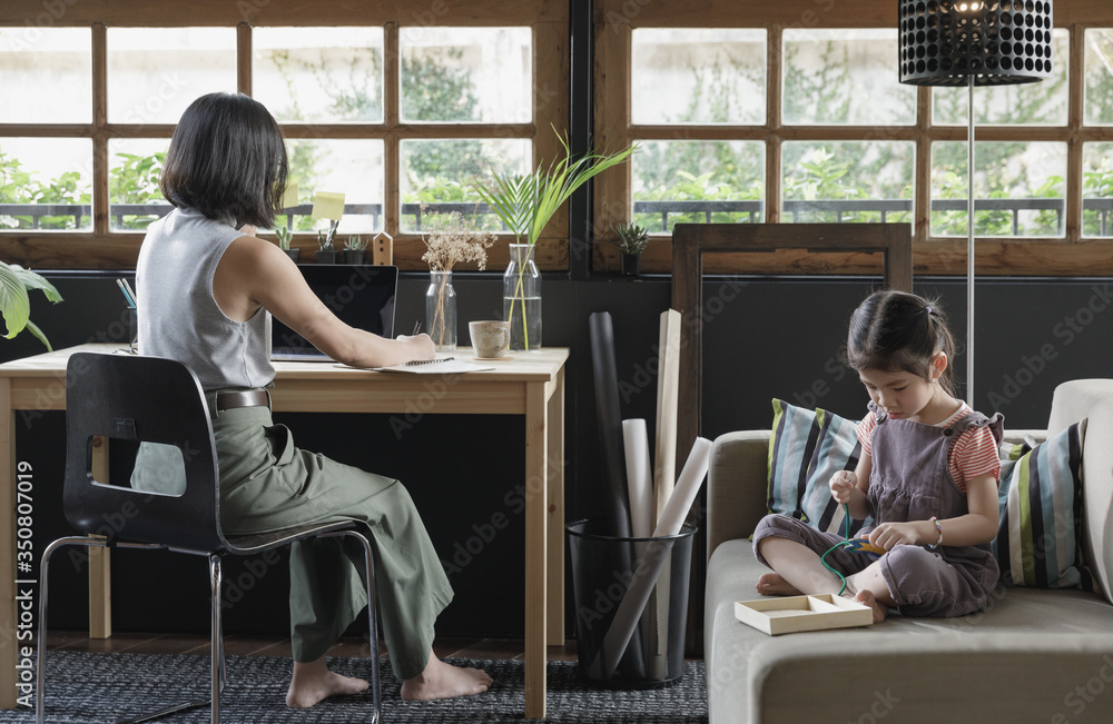 Working from home lifestyle mom using smartphone on the desk and her child girl learning the toy on sofa in the living room, Quarantine isolation during the Coronavirus (COVID-19) health crisis Working from home lifestyle mom using smartphone on the desk and her child girl learning the toy on sofa in the living room, Quarantine isolation during the Coronavirus (COVID-19) health crisis