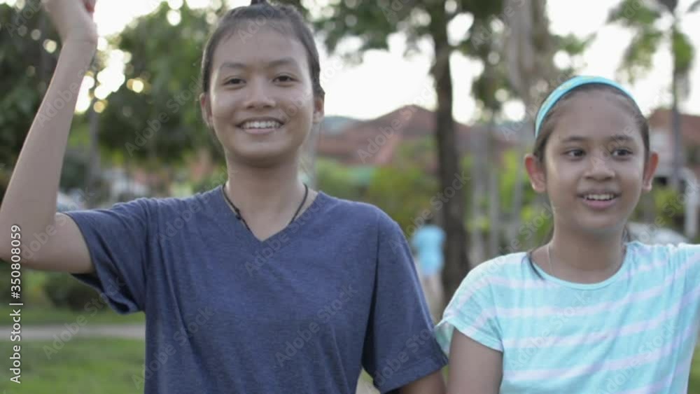 Two pretty asian girls are practicing dancing happily together at public park under sunlight. Cheerful female teenager and her sister in casual dress showing funny dance in residential area. Two pretty asian girls are practicing dancing happily together at public park under sunlight. Cheerful female teenager and her sister in casual dress showing funny dance in residential area.