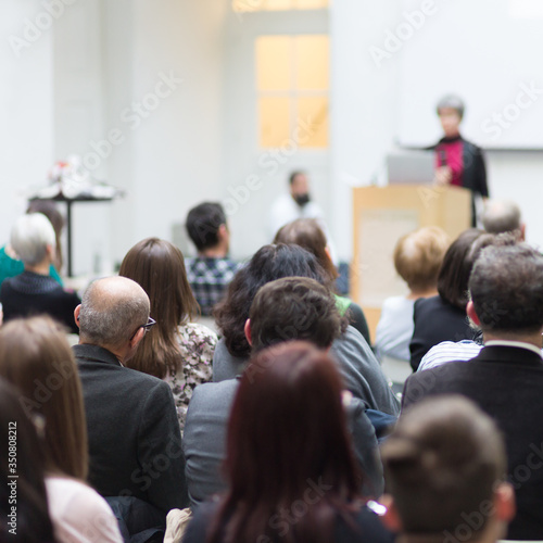 Business and entrepreneurship symposium. Female speaker giving a talk at business meeting. Audience in conference hall. Rear view of unrecognized participant in audience. © kasto