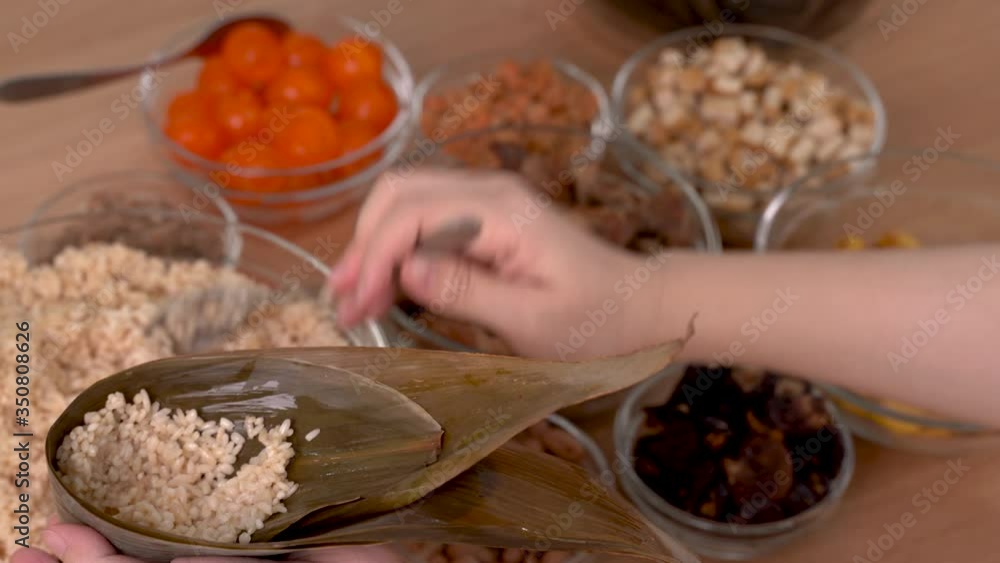 Making rice dumpling zongzi - family preparing, wrapping bunch of Chinese food together on wooden table at home for Dragon Boat Festival celebration, close up, lifestyle. Making rice dumpling zongzi - family preparing, wrapping bunch of Chinese food together on wooden table at home for Dragon Boat Festival celebration, close up, lifestyle.