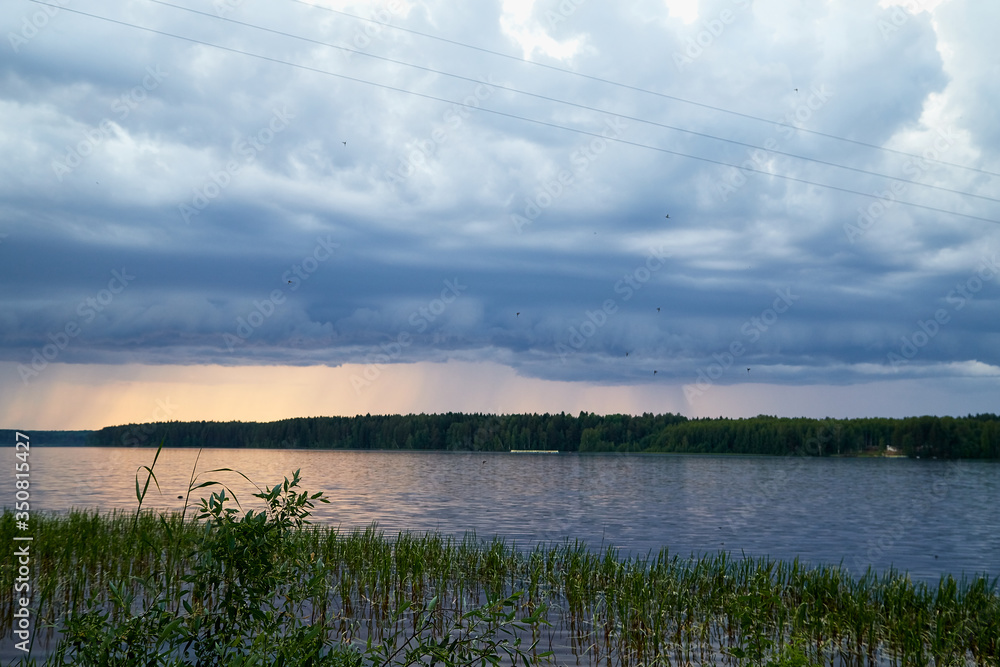 Beautiful landscape with lake, sky and clouds, rain and sunset on the horizon on background and green glass on foreground