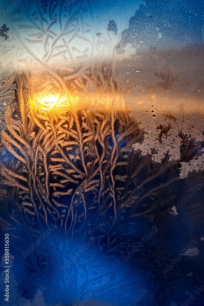 The light of the setting sun through the frosty pattern on the glass in winter