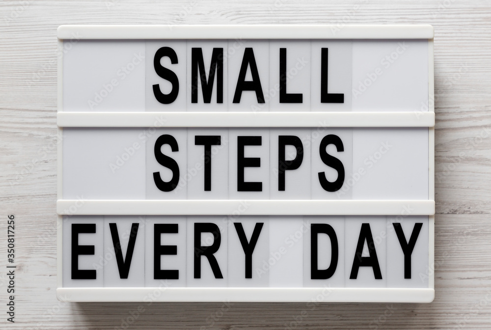 'Small steps every day' words on a lightbox on a white wooden surface, top view. Overhead, from above, flat lay. Close-up.