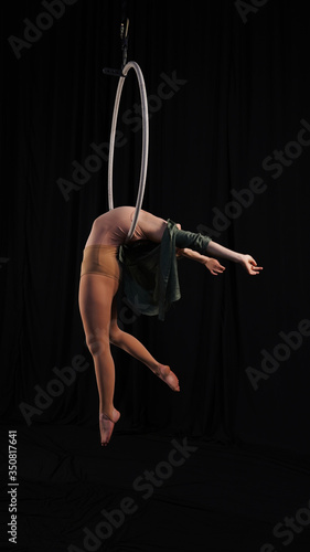 Girl aerialist flexibility, modern dance on a hoop, graceful flexible model, aerialist on circus props perform a dance, slim slim model in a beige suit