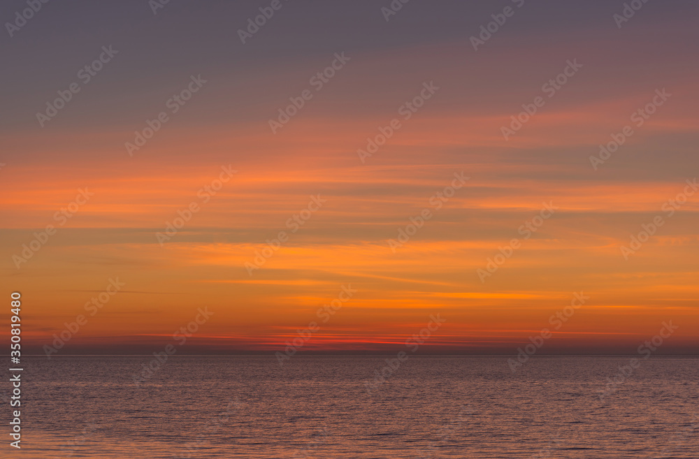 Bright twilight sunset sky over the sea. Wonderful sky after sunset in orange shades. The natural background. Purple hue of the sea and sky. Abstract lines of fire clouds.