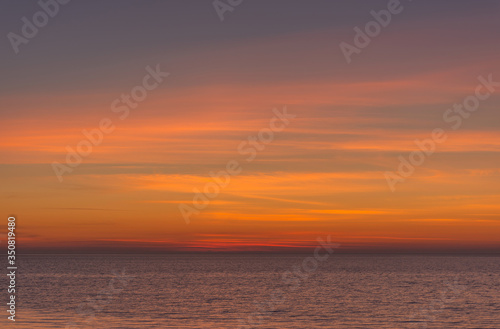 Bright twilight sunset sky over the sea. Wonderful sky after sunset in orange shades. The natural background. Purple hue of the sea and sky. Abstract lines of fire clouds.