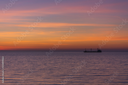 Bright twilight sunset sky over the sea. Wonderful sky after sunset in orange shades. The natural background. Purple hue of the sea and sky. Abstract lines of fire clouds. A ship on the horizon. © Anna Pismenskova