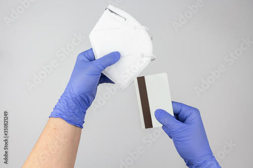 Hands with protective gloves holding a face mask and a credit card
