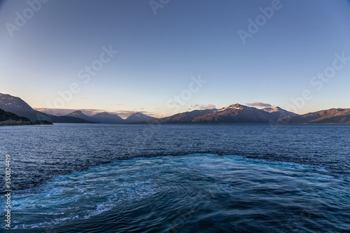 A mystical fjord in Norway with mountains and fog hanging over the water in polar day. midnight sun, selective focus