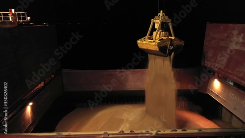 Nighttime close-up of cargo bulker anchored in seaport during loading grain on ship. Gantry crane drop agricultural crops, bulk commodities to ship hold storage, merchant carrier boat preparation