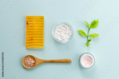 Organic cosmetics with natural ingredients: soap, face cream, alginate mask, sea salt on light blue background, top view