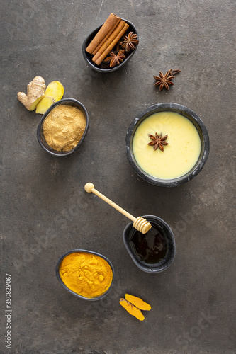 Golden milk drink and ingredients ginger, turmeric, spices and milk on concrete background. This Ayurvedic warm beverage has multiple health benefits.Top view