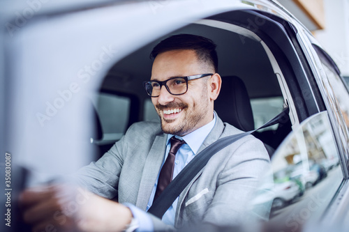 Attractive caucasian smiling elegant unshaven businessman in suit and eyeglasses driving his expensive car. © dusanpetkovic1