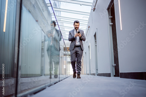 Full length of handsome Caucasian positive businessman going to a meeting with architects. He is reading important e-mail from his business partners. Hall of building in construction process interior. © dusanpetkovic1