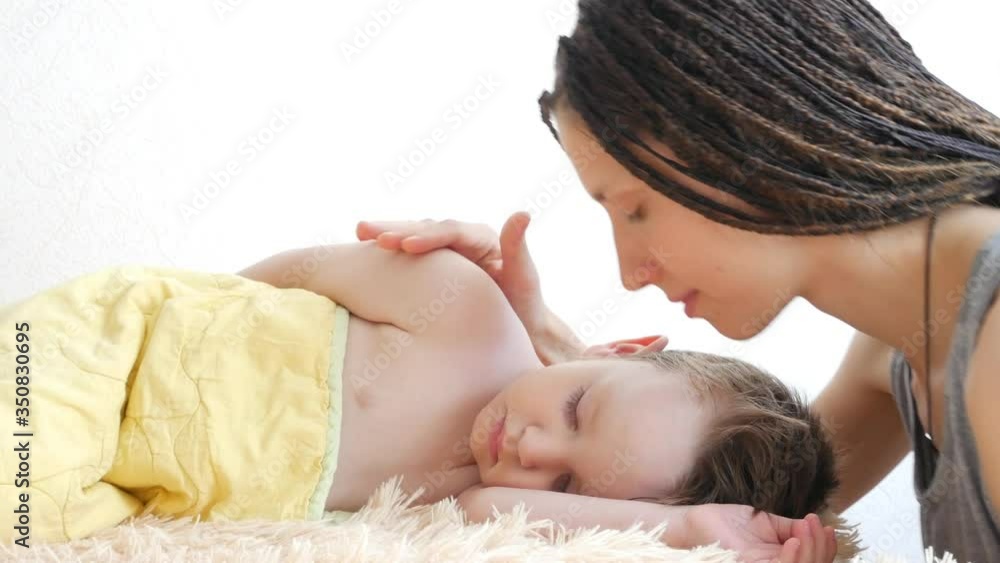 A young braids woman caresses and kisses her lovely sleeping son A young braids woman caresses and kisses her lovely sleeping son