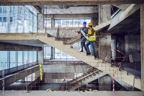 Construction worker and main architect climbing the stairs and talking about progress in construction of new building.