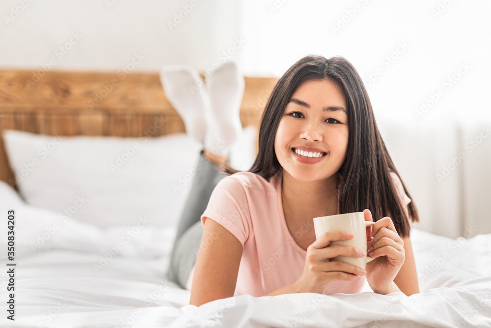 Asian Girl Having Coffee Lying In Bed In Cozy Bedroom