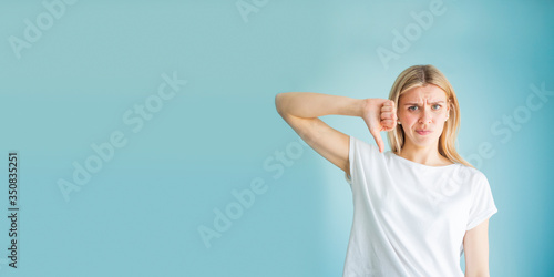 Unhappy European woman giving thumb down gesture looking with negative expression and disapproval. Studio photo on a blue background. Wide banner copy space © woodpencil