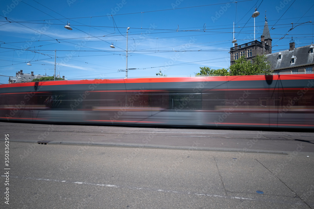 A moving tram at day, houses in background, blue sky, in long exposure. The Hague, the Netherlands