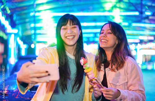 Canvas Print Happy asian girls eating candy sweets and taking selfie at amusement park - Youn