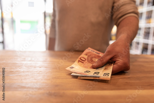 Paying cash money in euro’s by placing the money on a counter in a retail shop. A mans hand holding the banknotes in his hand. Bokeh background