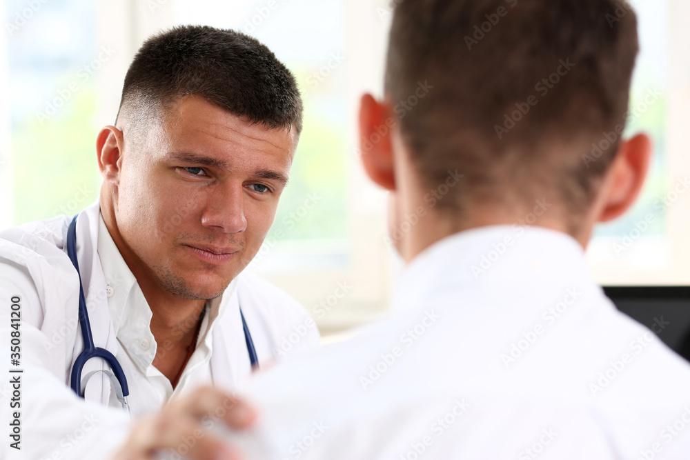 Fototapeta premium Friendly male doctor hold patient shoulder in office during reception