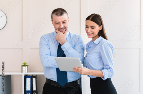 Businesswoman Showing Tablet Computer To Colleague Businessman Standing In Office