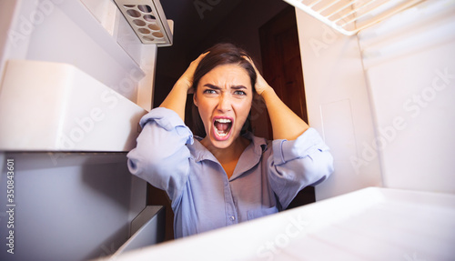 Panicked woman looking at empty shelves of her refrigerator