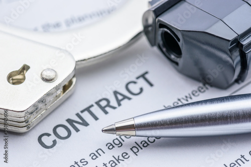 Pen, a pistol and a handcuff on a contract form, depicting a contract was signed by a coerced or forced person at gunpoint. photo