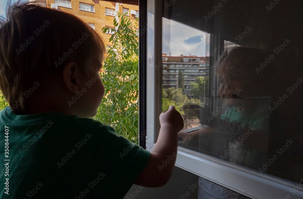 boy looking at the street through his window and his reflection in the glass
boy looking at the street through his window and his reflection in the glass