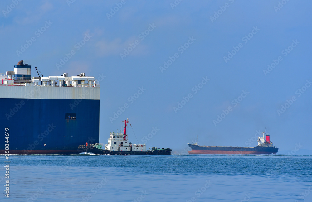 Stern of a large tanker cargo ship on route to sailing in the sea by there is a towing tugboat to assistance tow Thailand