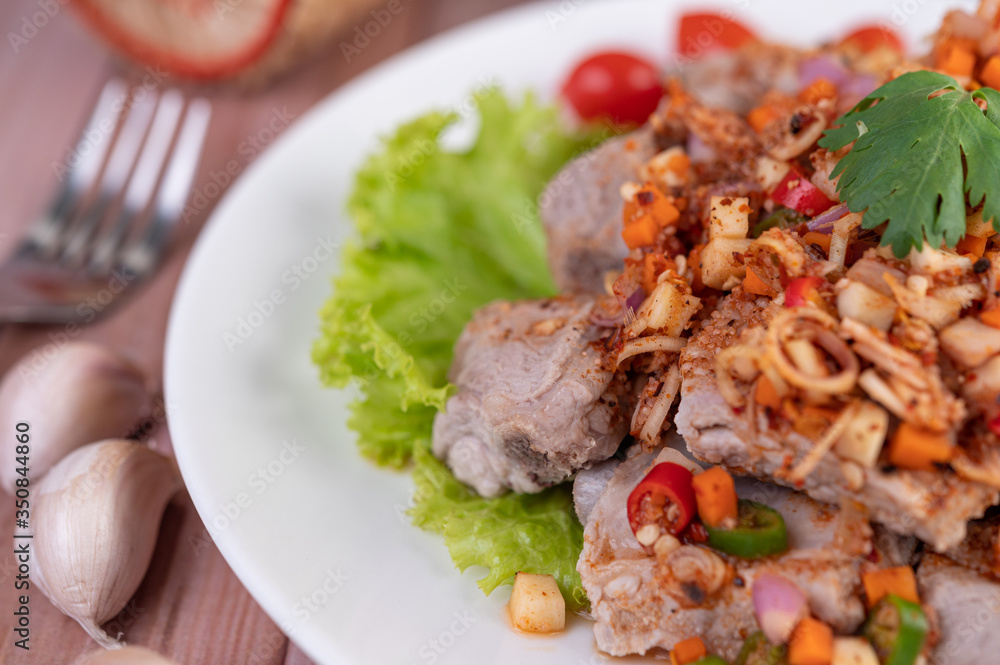 Spicy pork minced with tomatoes and lettuce on a white plate on a wooden table. Spicy pork minced with tomatoes and lettuce on a white plate on a wooden table.