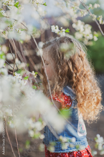 Cute little girl with curly hair in a flowering garden