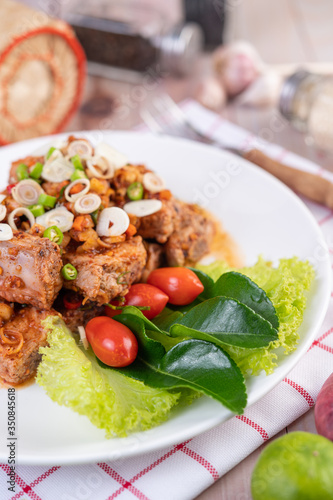 Spicy pork minced with tomatoes and lettuce on a white plate on a wooden table.