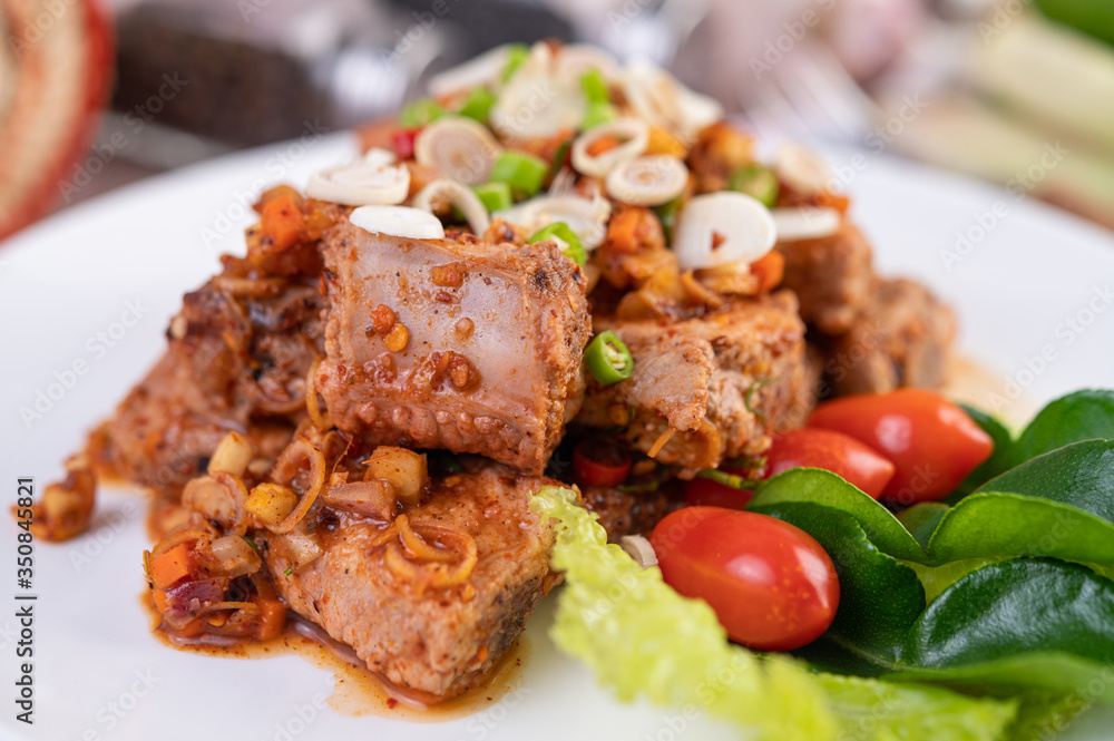 Spicy pork minced with tomatoes and lettuce on a white plate on a wooden table. Spicy pork minced with tomatoes and lettuce on a white plate on a wooden table.