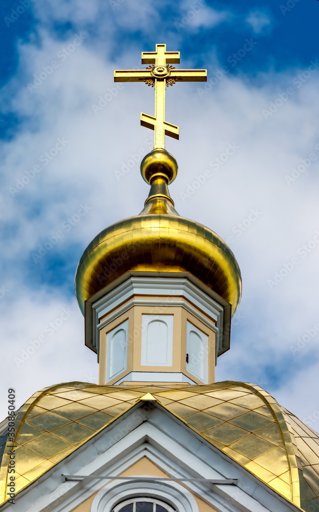Gilded dome of the Orthodox Church against the blue sky with clouds in summer closeup