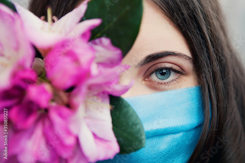 Young beautiful woman in medical mask with spring flowers, stay isolation at home for self quarantine. Concept home quarantine, prevention COVID-19, Coronavirus outbreak situation, positive thinking