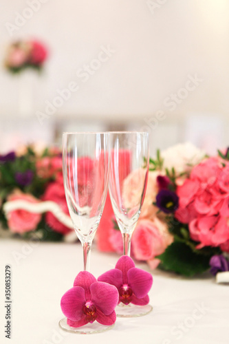 Wedding glasses decorated with live orchids on a background decorated with flower arrangements table
