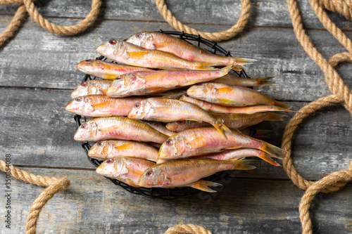 Black sea fish, red mullet in a black bowl on a gray wooden table. A lot of barabulka fish. Top view with space for text