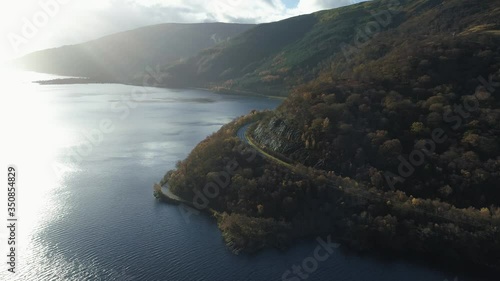 Beautiful road bends around at the base of a mountain. Loch Lomand, Scotland, sky reflects off of large lake photo