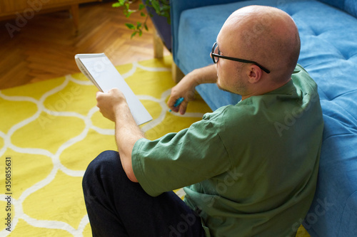 Young man in casual clothes sitiing in a living room and holding a notebook photo