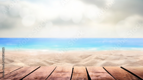 Fototapeta Naklejka Na Ścianę i Meble -  A wooden table product display with a summer vacation, holiday background of a tropical beach and blue sea and white fluffy clouds and sun flare.