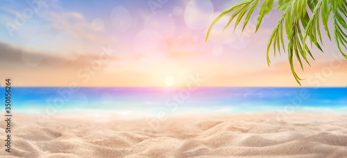 Fototapeta Naklejka Na Ścianę i Meble -  A summer vacation, holiday background of a tropical beach and blue sea at sunset with the sun on the horizon with bokeh and palm trees.