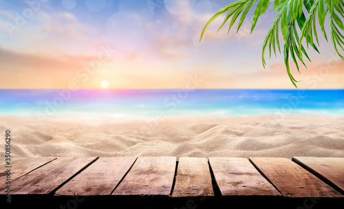 A wooden table product display with a summer vacation, holiday background of a tropical beach and blue sea at sunset with the sun on the horizon with bokeh and palm trees.