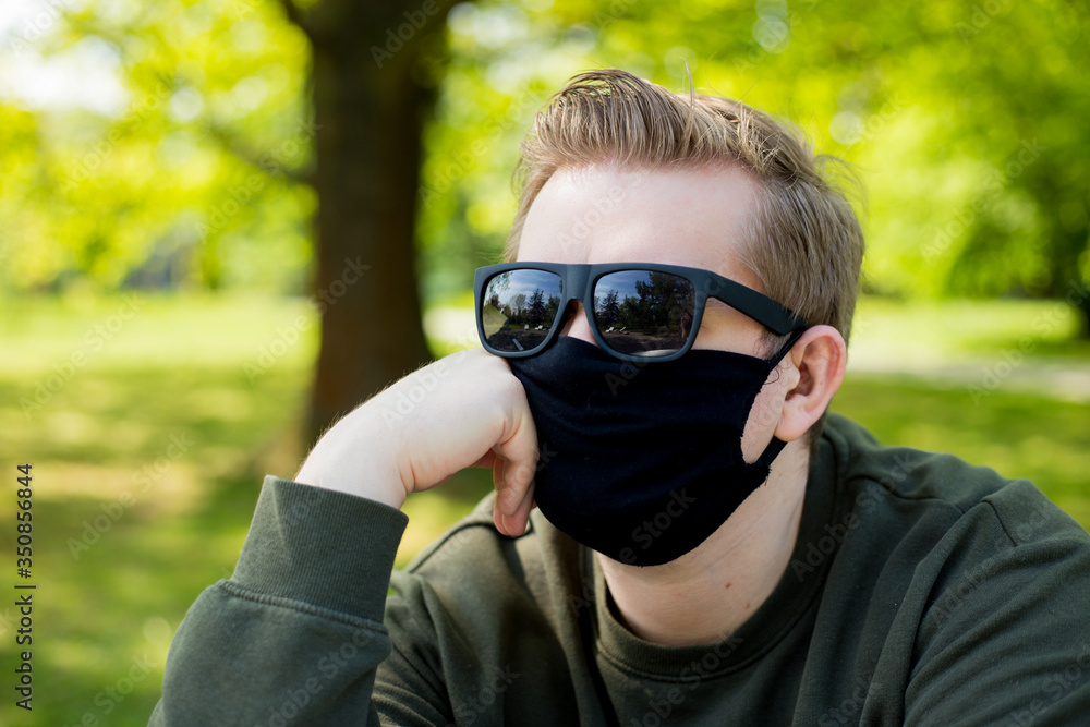 Portrait of a sick sadness man wearing medical mask on a city public park bacground. Corona virus pandemic. Concept Of Air pollution, Pneumonia Outbreak, smog or Epidemic Portrait of a sick sadness man wearing medical mask on a city public park bacground. Corona virus pandemic. Concept Of Air pollution, Pneumonia Outbreak, smog or Epidemic