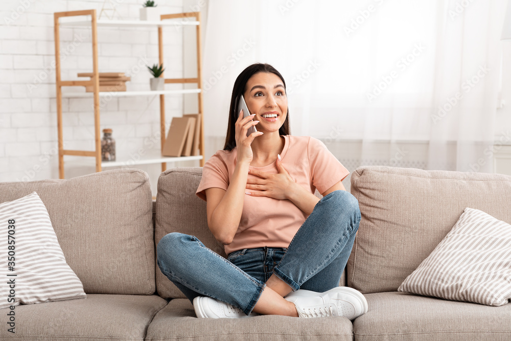 Obraz premium Excited woman talking on mobile phone sitting on couch