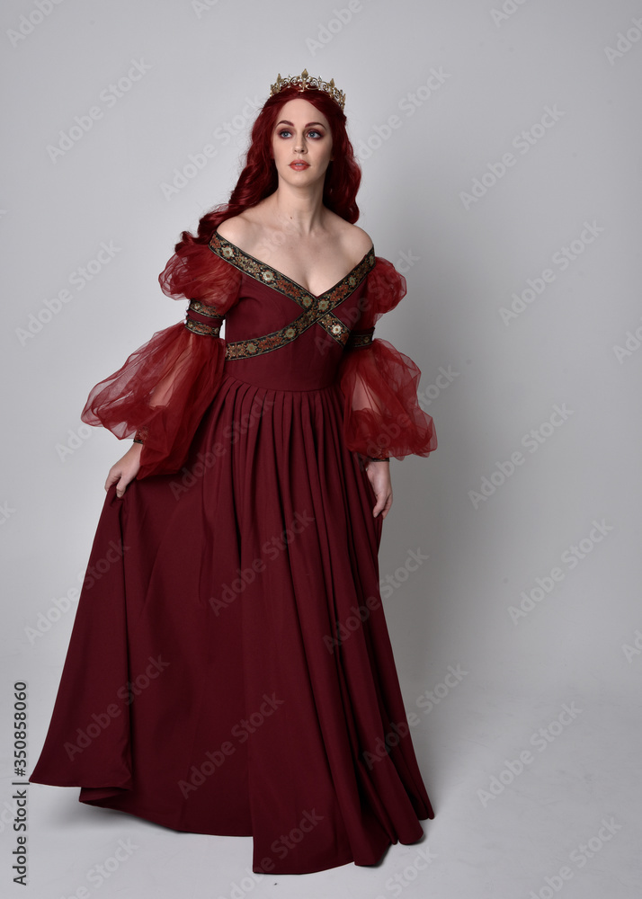 Portrait of a beautiful woman with red hair wearing a flowing Burgundy fantasy gown and golden crown. full length standing pose, isolated against a studio background
Portrait of a beautiful woman with red hair wearing a flowing Burgundy fantasy gown and golden crown. full length standing pose, isolated against a studio background