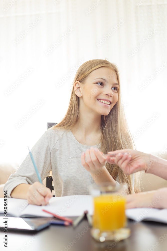 Smiling happy teenage Caucasian girl doing homework in living room, being helped by her mother Smiling happy teenage Caucasian girl doing homework in living room, being helped by her mother