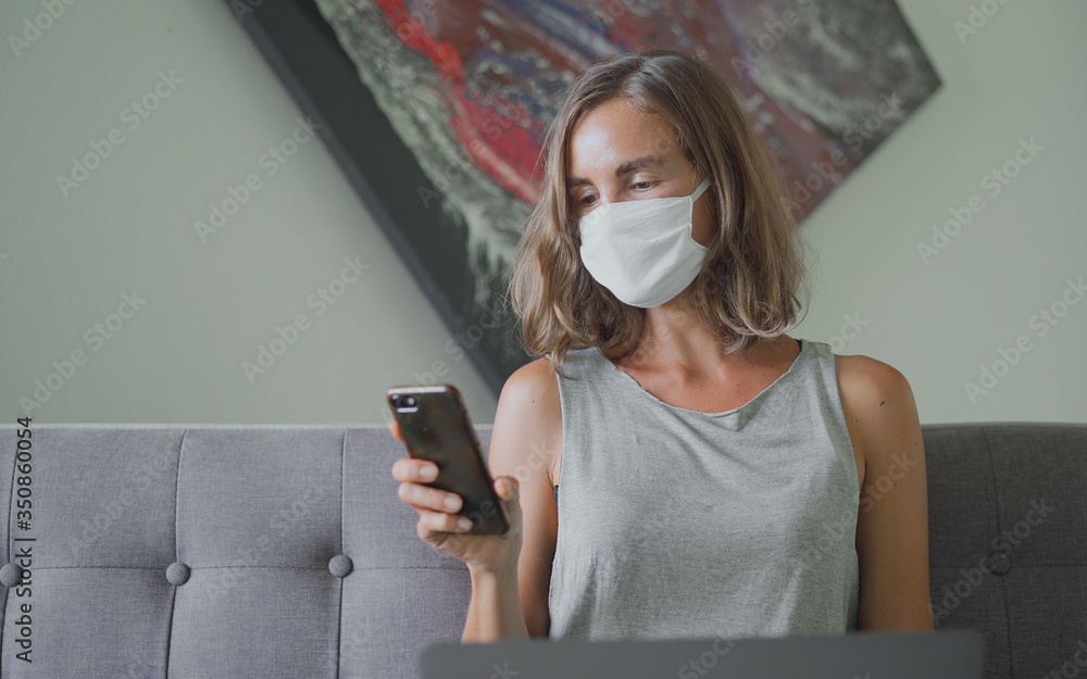 Woman wearing protective mask watching on smartphone sitting on sofa.jpg

