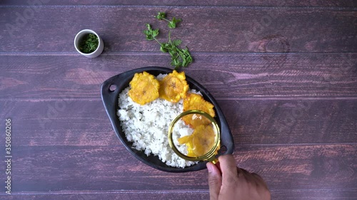 Above view of a black man’s hand using a magnifying glass to inspect an artisanal plate of rice with fried plantains on a table